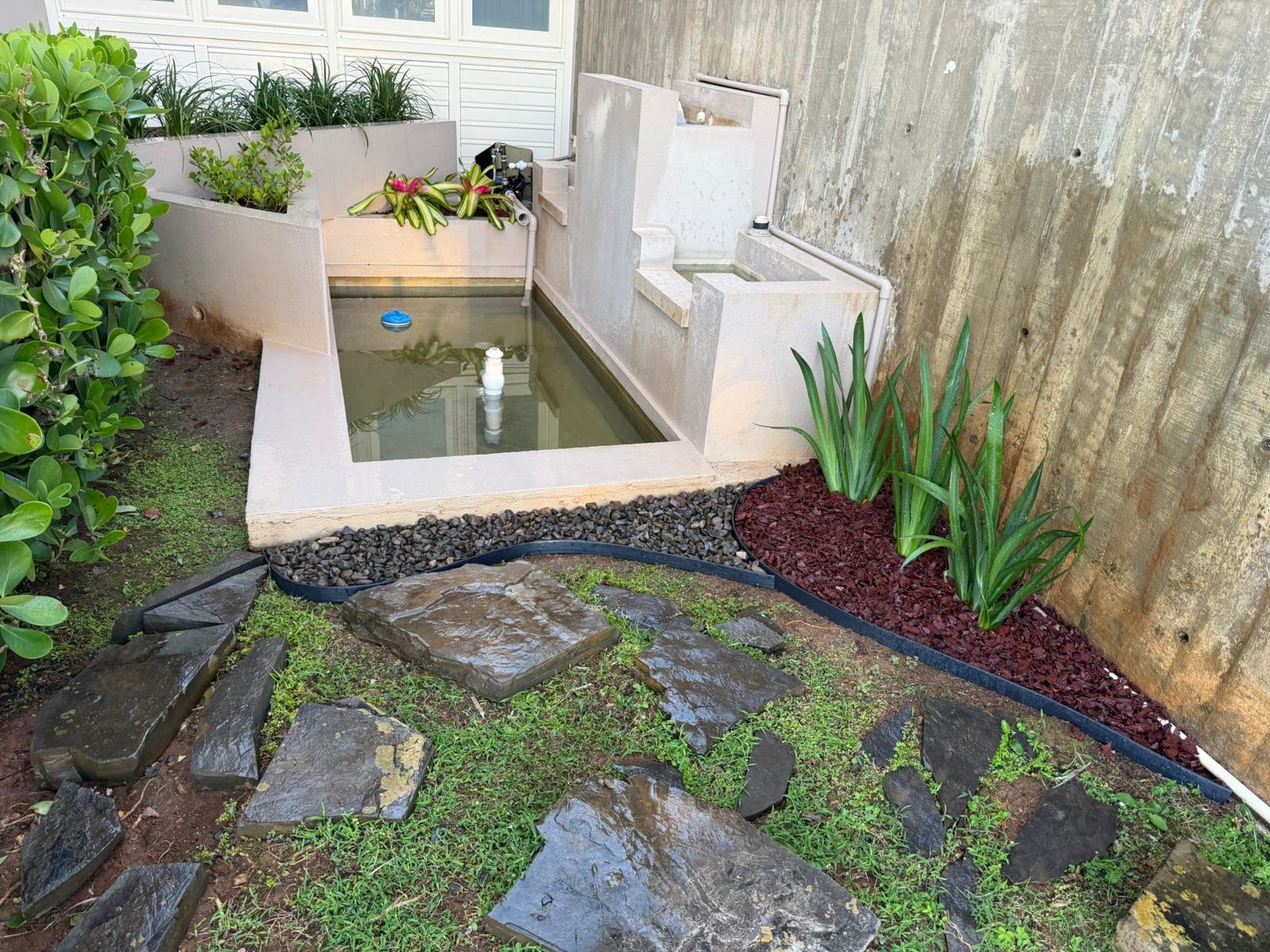 Estanque con fuente, piedra de río y mulch rojo en patio residencial